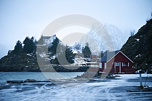 Typical scandinavian red house at fjord in front of snow covered mountains in winter