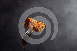 Typical spanish croqueta on a fork with copy space and dark background. photo