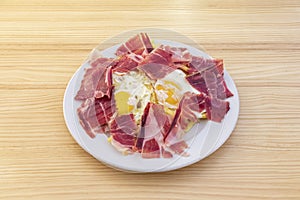 Typical spanish dish of broken eggs with serrano ham on a portion of fried potatoes