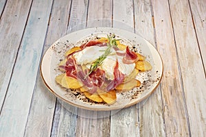 Typical Spanish dish to share with broken fried eggs with Iberian ham and homemade chips topped with a rosemary branch