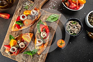 Typical spanish pincho Anchovies with tomato on bread on a dark background. top view. copy space for text