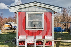 A typical Swedish red summerhouse with a square window, white chairs and wooden facade. The bare exterior has a simple aspect