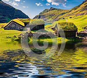 Typical turf-top houses reflected in calm waters of small pond in Saksun village, Faroe Islands.