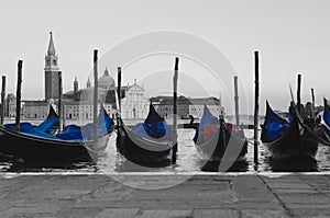 Typical Venetian boats for tourists in St. Mark`s Square in Venice. Black and white background keeping the blue tarps of the boat