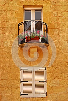 Typical window design and balcony grill with flower pot on brick wall at a triq in Mdina, Malta