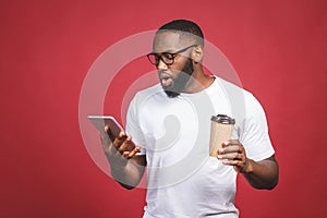 Typing a message. Surprised black man typing something on the mobile phone, drinking coffee while standing isolated against red