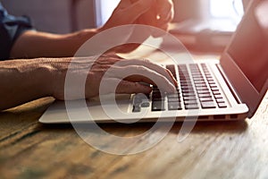 Typing on notebook computer, close up of hands of business man working on laptop. Side view, selective focus