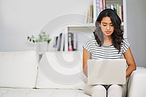 Typing up a new article for her blog. a young woman using her laptop while relaxing on her sofa at home.