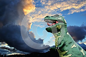 Tyrannosaurus-rex model against a sunset sky with storm clouds