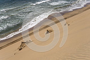 tyre tracks on shore with dune slope and Atlantic waves near Sandwich Harbour, Namibia