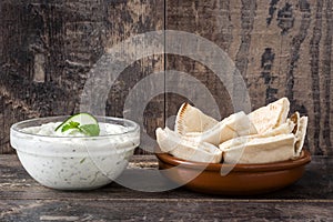 Tzatziki sauce in bowl and pita bread on rustic wooden table