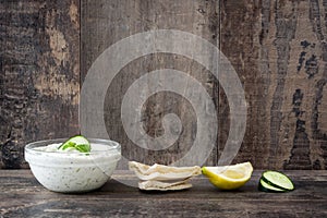 Tzatziki sauce in bowl and pita bread on rustic wooden table