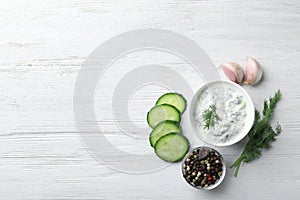 Tzatziki sauce in bowl with slices of cucumber, garlic, pepper and dill on white wooden background, top view.