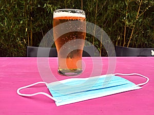 U.K. pubs and bars reopening on July 4th concept with Coronavirus covid-19 face mask on table next to a pint of lager  or beer
