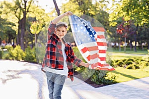 U.S. Independence Day. A young guy American or caucasian, 8 years old riding at the speed on a skateboard. Holding the fluttering