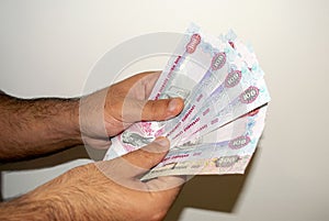 UAE national currency. UAE money banknotes. A young man holds in his hands` dirhams on light white background
