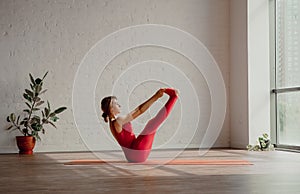 ubhaya padangushthasana. Young womanin red sports overalls is doing yoga in the studio. Healthy lifestyle concept