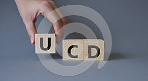 UCD - User Centered Design. Wooden cubes with word UCD. Businessman hand. Beautiful grey background. Business and User Centered