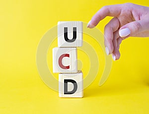 UCD - User Centered Design. Wooden cubes with word UCD. Businessman hand. Beautiful yellow background. Business and User Centered