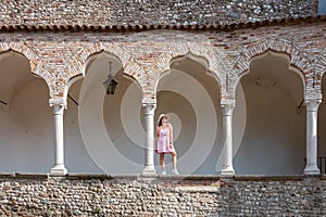 Udine - Female model standing between columns and arches of renaissance Venetian gothic style arcade
