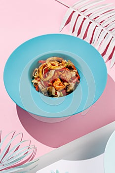 Udon with calamary and vegetables, seafood on blue pastel color plate at white background with sunlight and shadows, minimalism,