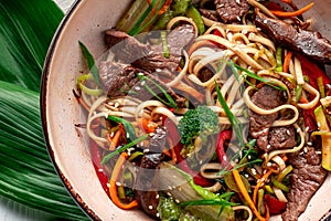 Udon stir fry noodles with beef meat and vegetables in a plate on white wooden background