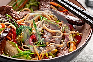 Udon stir fry noodles with beef meat and vegetables in a plate on white wooden background