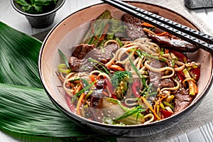 Udon stir fry noodles with beef meat and vegetables in a plate on white wooden background