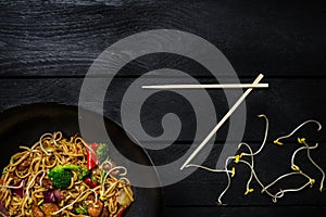 Udon stir fry noodles with chicken and vegetables in wok pan on black wooden background. With chopsticks