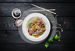 Udon stir fry noodles with meat or chicken and vegetables in a white plate with chopsticks.