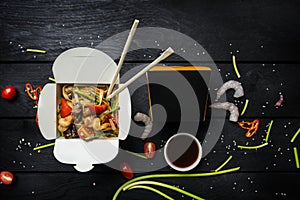 Udon stir fry noodles with seafood in a box on black background. With chopsticks and box for noodles.