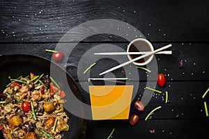 Udon stir fry noodles with seafood and vegetables in wok pan on black wooden background. With a box for noodles