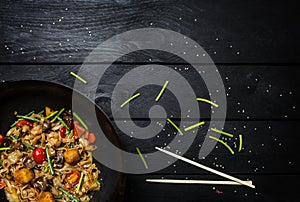 Udon stir fry noodles with seafood and vegetables in wok pan on black wooden background. With a box for noodles