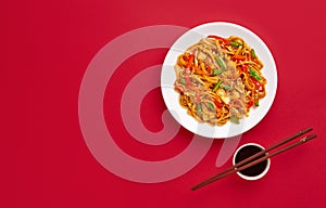 Udon stir fry noodles with vegetables. Asian vegan vegetarian food over red background, flat lay