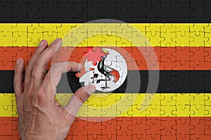 Uganda flag is depicted on a puzzle, which the man`s hand completes to fold