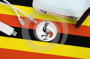 Uganda flag depicted on table with internet rj45 cable, wireless usb wifi adapter and router. Internet connection concept