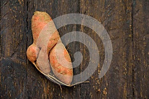 Ugly food. Deformed organic carrot on wooden background. Misshapen produce, food waste problem concept. Minimal style. Flat lay.