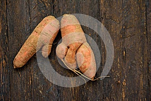 Ugly food. Deformed organic carrot on wooden background. Misshapen produce, food waste problem concept. Minimal style. Flat lay.