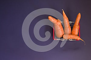 Ugly food. Deformed organic carrots on a purple background. Food waste concept in food basket. Minimalism, pop art. Flat lay