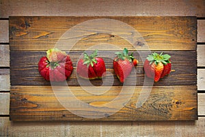 Ugly food. Strange deformed strawberries on wooden background. Misshapen produce, food waste problem concept. photo