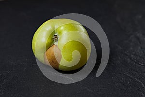 An ugly fruit. Green apple with a spot on a dark background. Concept - Food waste reduction. Using in cooking imperfect products