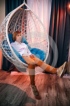 Ugly girl in a white shirt and red jeans on a white wicker hanging chair