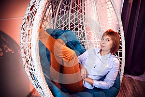 Ugly girl in a white shirt and red jeans on a white wicker hanging chair