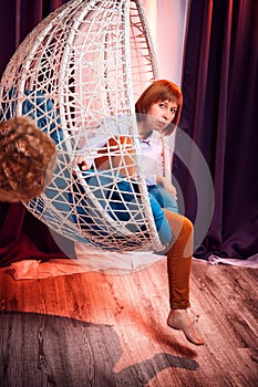 Ugly girl in a white shirt and red jeans on a white wicker hanging chair