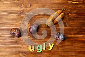 Ugly organic blue plums and carrot on wooden background. The ugly produce trend is the sale of imperfect looking produce