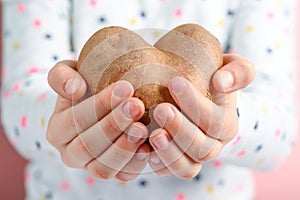 Ugly potato in the shape of a heart in children`s hands.