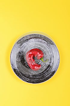 Ugly red chili peppers on a black plate on a yellow background, minimal style of nature, pop art, creative food concept, modern