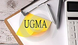 UGMA - Uniform Gifts to Minors Act word on a yellow sticky with calculator, pen and clipboard