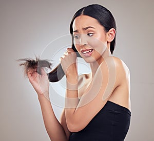 Uh oh Split ends. an attractive young woman holding her hair and looking worried while posing in the studio.