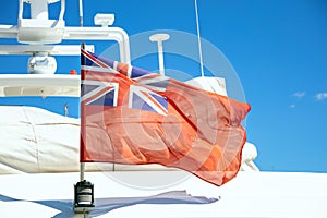 UK flag on pole on ferry`s stern. Ongoing cruise to islands. Blue sky background